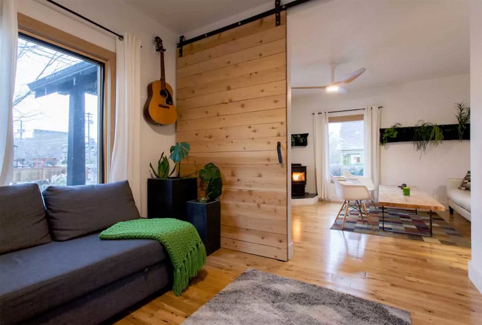 Ejemplo de sala de estar abierta contemporánea pequeña con paredes blancas, suelo de madera clara, chimenea de esquina y marco de chimenea de yeso
