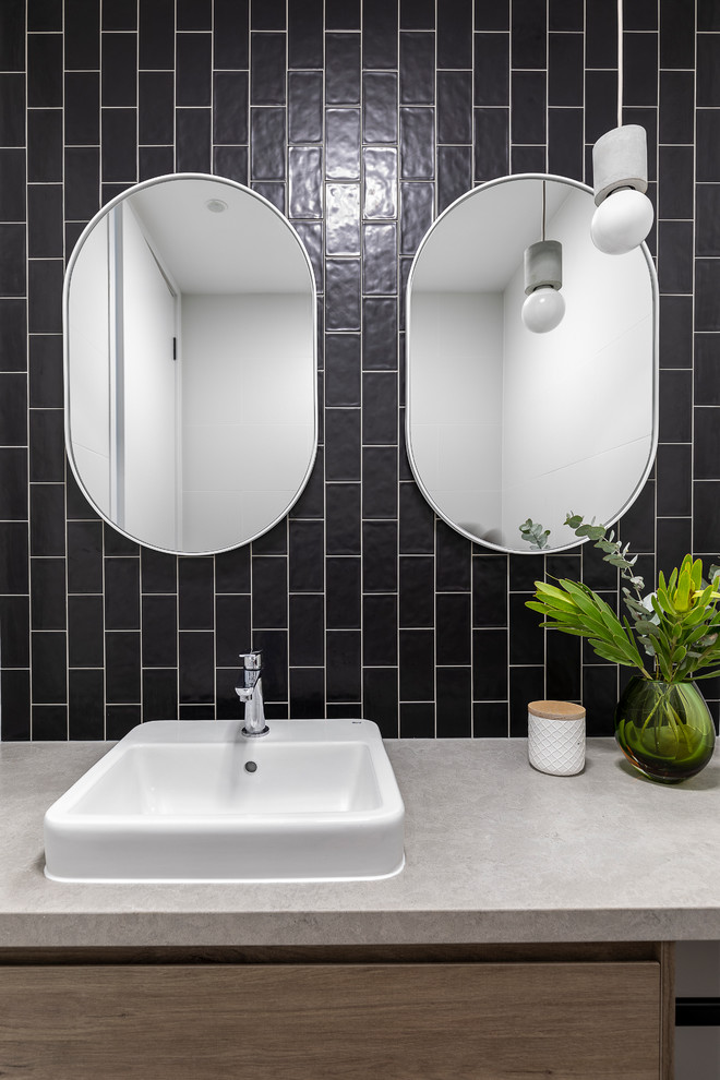 This is an example of a mid-sized contemporary powder room in Brisbane with furniture-like cabinets, medium wood cabinets, a one-piece toilet, black and white tile, ceramic tile, black walls, a vessel sink, engineered quartz benchtops, grey floor and grey benchtops.