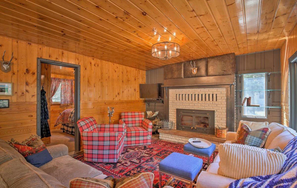 Photo of a mid-sized country open concept family room in Other with brown walls, light hardwood floors, a standard fireplace, a brick fireplace surround, a wall-mounted tv and grey floor.