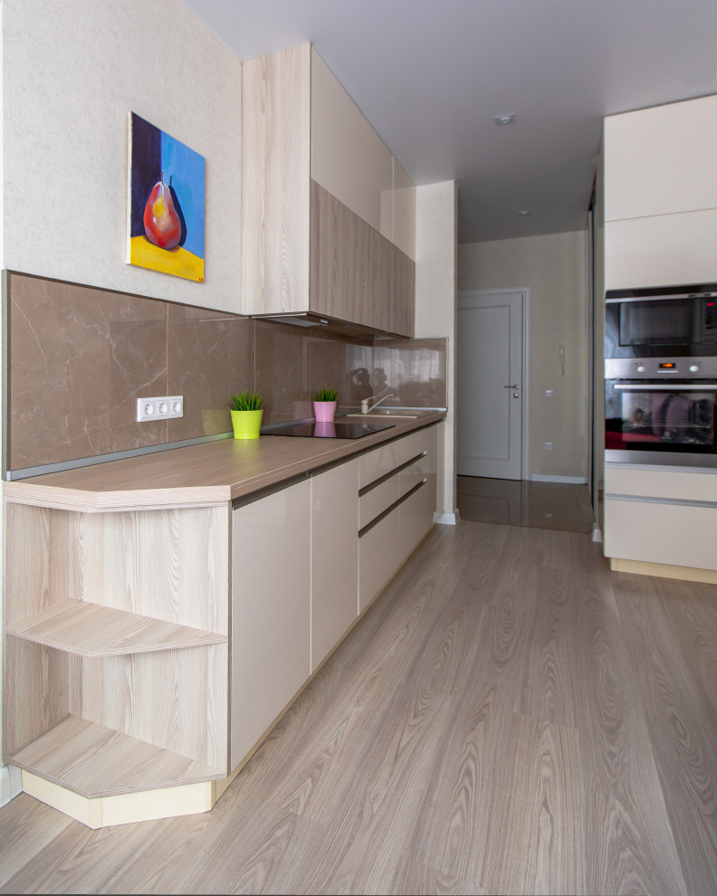 This is an example of a mid-sized contemporary galley open plan kitchen in Saint Petersburg with an undermount sink, flat-panel cabinets, beige cabinets, laminate benchtops, beige splashback, porcelain splashback, black appliances, laminate floors, beige floor and beige benchtop.