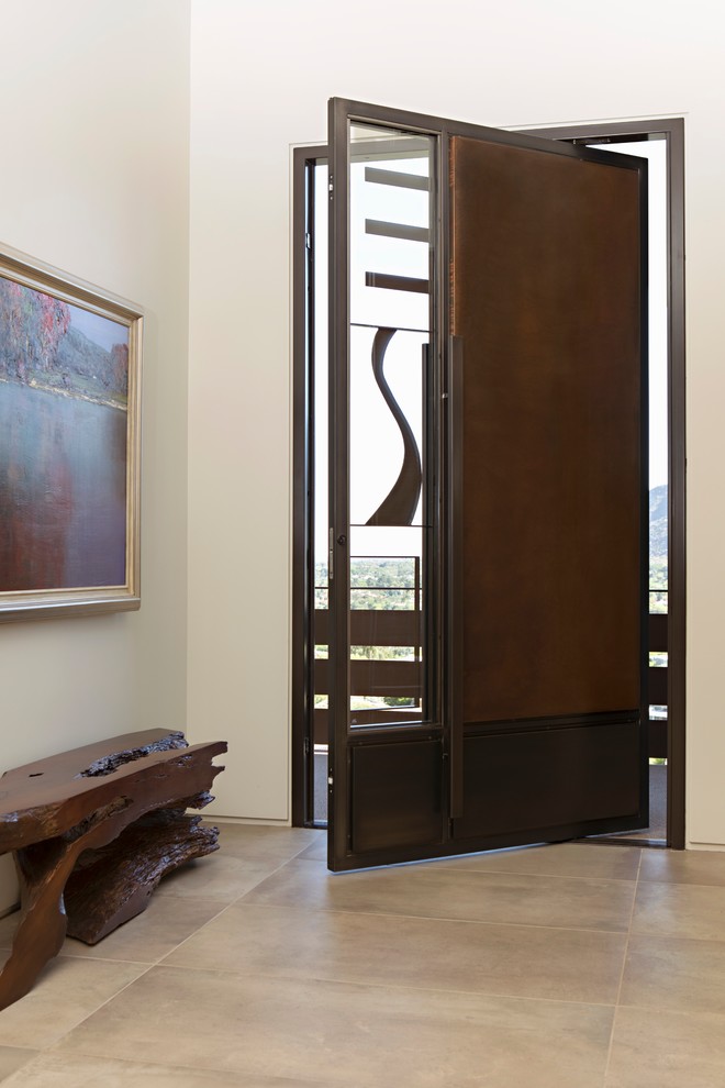 This is an example of a large modern front door in Phoenix with beige walls, limestone floors, a pivot front door, a dark wood front door and beige floor.