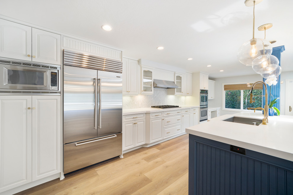 Example of a mid-sized transitional laminate floor and brown floor eat-in kitchen design in Orange County with an undermount sink, shaker cabinets, blue cabinets, quartz countertops, white backsplash, mosaic tile backsplash, stainless steel appliances, an island and white countertops