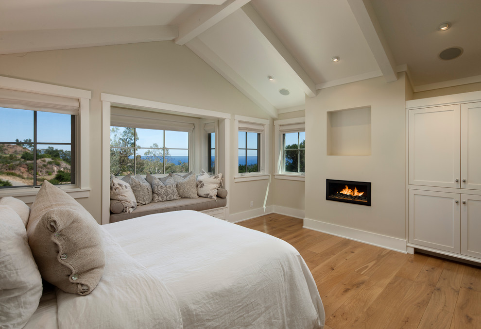 Design ideas for a large traditional master bedroom in Santa Barbara with a ribbon fireplace, beige walls, medium hardwood floors and a plaster fireplace surround.