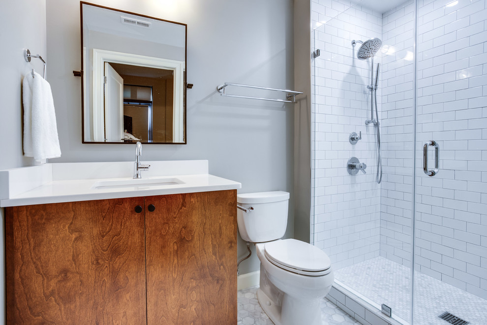 Modern 3/4 bathroom in DC Metro with furniture-like cabinets, brown cabinets, an alcove shower, a two-piece toilet, white tile, porcelain tile, grey walls, marble floors, an undermount sink, engineered quartz benchtops, a hinged shower door and white benchtops.