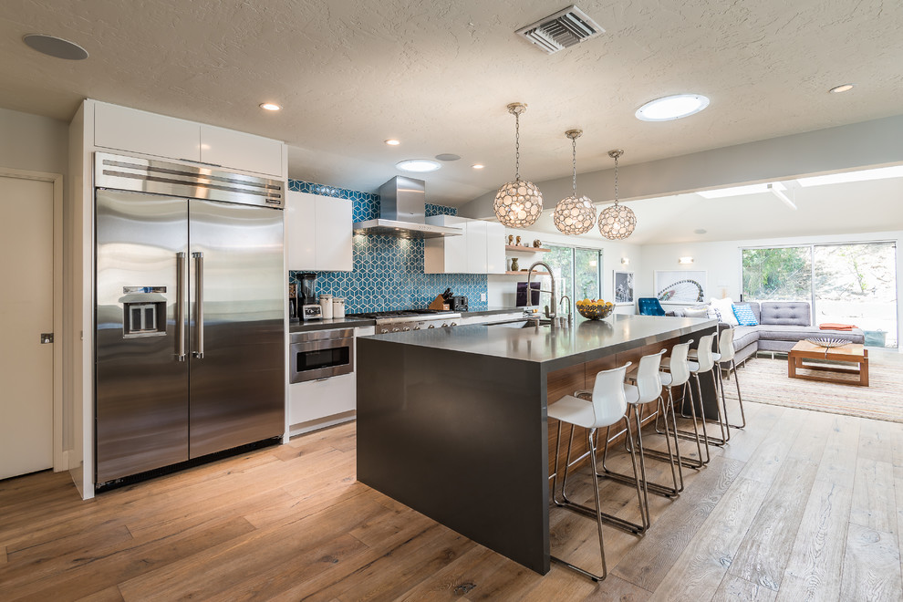 This is an example of a large contemporary open plan kitchen in Los Angeles with an undermount sink, flat-panel cabinets, white cabinets, quartz benchtops, blue splashback, ceramic splashback, stainless steel appliances, medium hardwood floors and with island.