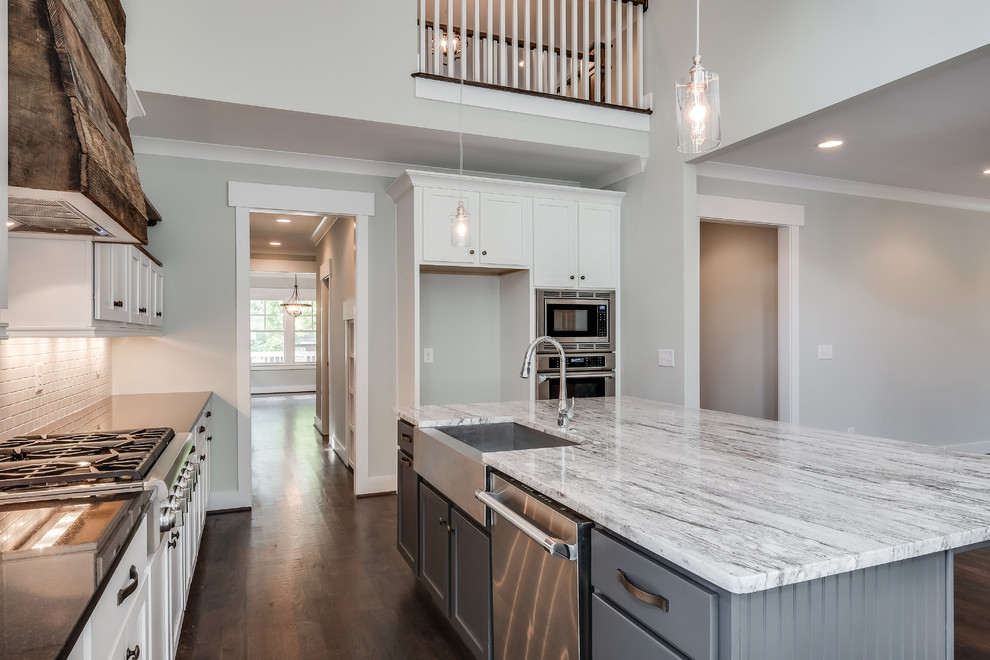 Design ideas for a mid-sized arts and crafts galley open plan kitchen in Nashville with a farmhouse sink, shaker cabinets, white cabinets, granite benchtops, white splashback, ceramic splashback, stainless steel appliances, dark hardwood floors and with island.