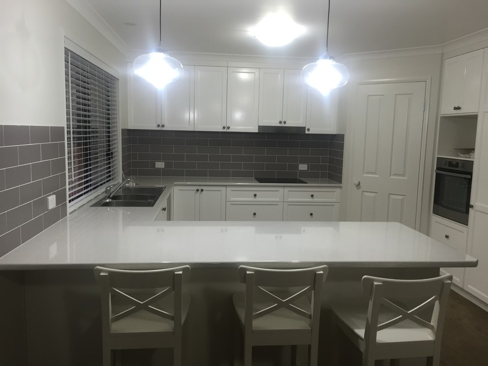 Photo of a transitional u-shaped kitchen in Brisbane with white cabinets, laminate benchtops and grey splashback.