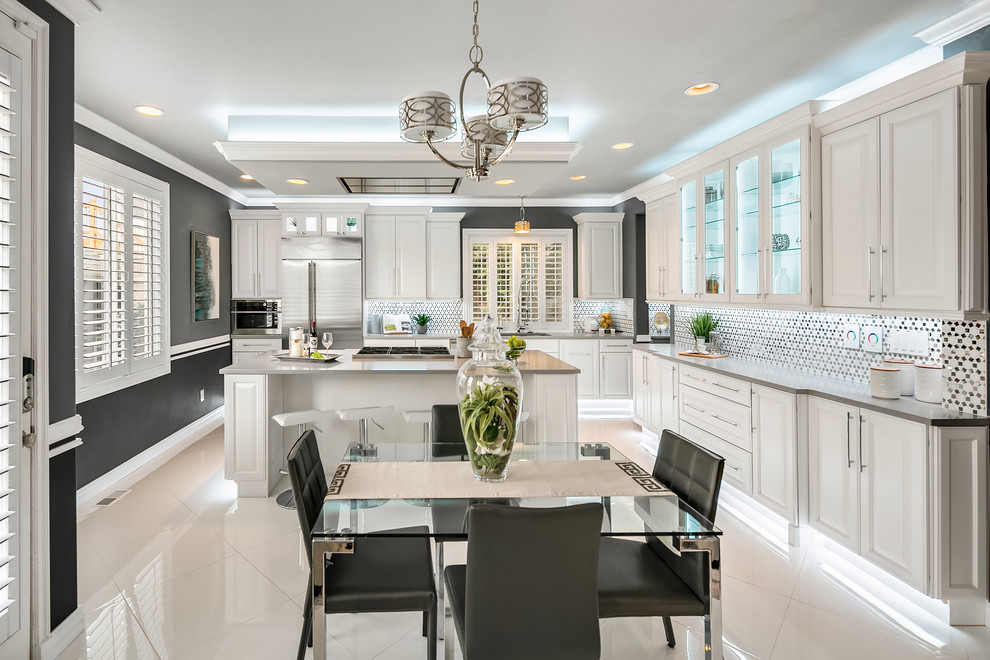 This is an example of a large transitional l-shaped eat-in kitchen in Seattle with an undermount sink, raised-panel cabinets, white cabinets, white splashback, stainless steel appliances, porcelain floors, with island, white floor and grey benchtop.