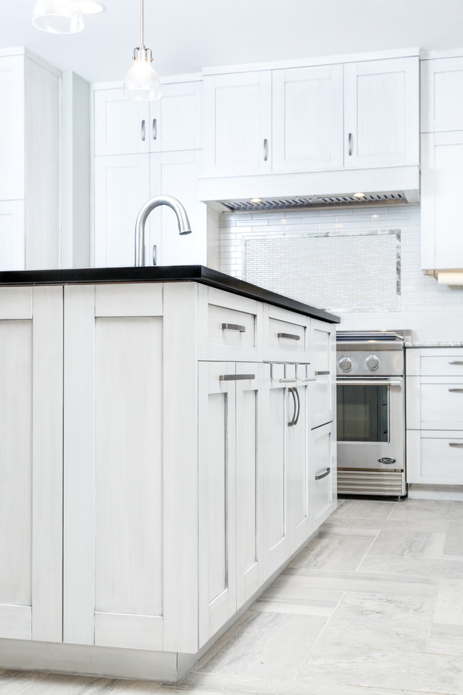Example of a large transitional l-shaped porcelain tile eat-in kitchen design in Austin with a single-bowl sink, shaker cabinets, gray cabinets, soapstone countertops, white backsplash, ceramic backsplash, stainless steel appliances and an island
