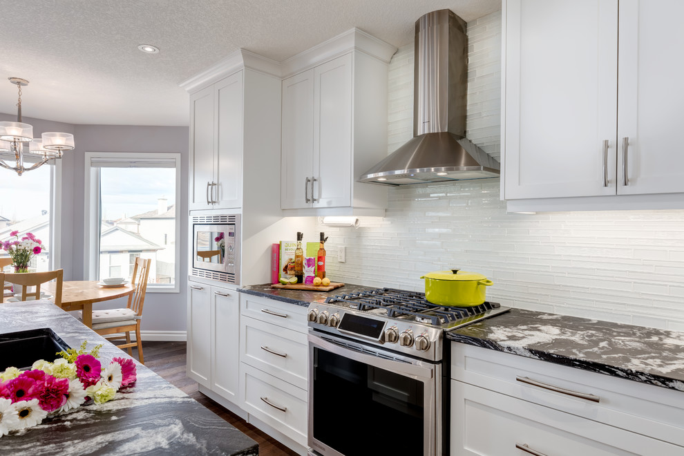 Transitional galley dark wood floor eat-in kitchen photo in Calgary with an undermount sink, shaker cabinets, white cabinets, marble countertops, white backsplash, glass tile backsplash and an island