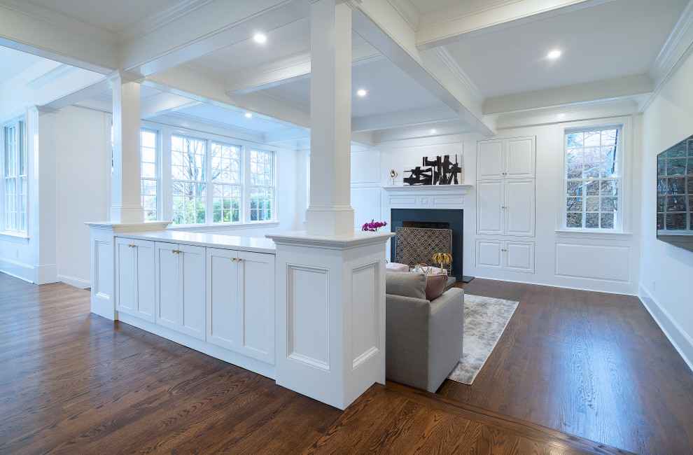 Large transitional open concept family room in Philadelphia with white walls, dark hardwood floors, a standard fireplace, a wood fireplace surround, a wall-mounted tv, brown floor, coffered and panelled walls.