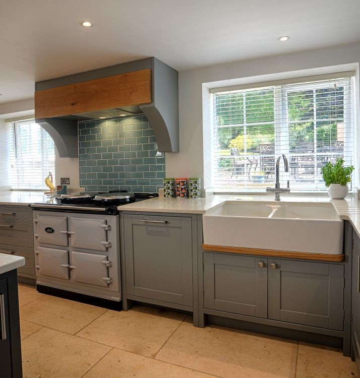 Large country open plan kitchen in Gloucestershire with a farmhouse sink, shaker cabinets, grey cabinets, granite benchtops, white splashback, stainless steel appliances, porcelain floors and a peninsula.