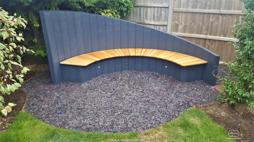 This is an example of a small contemporary backyard partial sun formal garden for summer in Cambridgeshire with a fire feature and river rock.