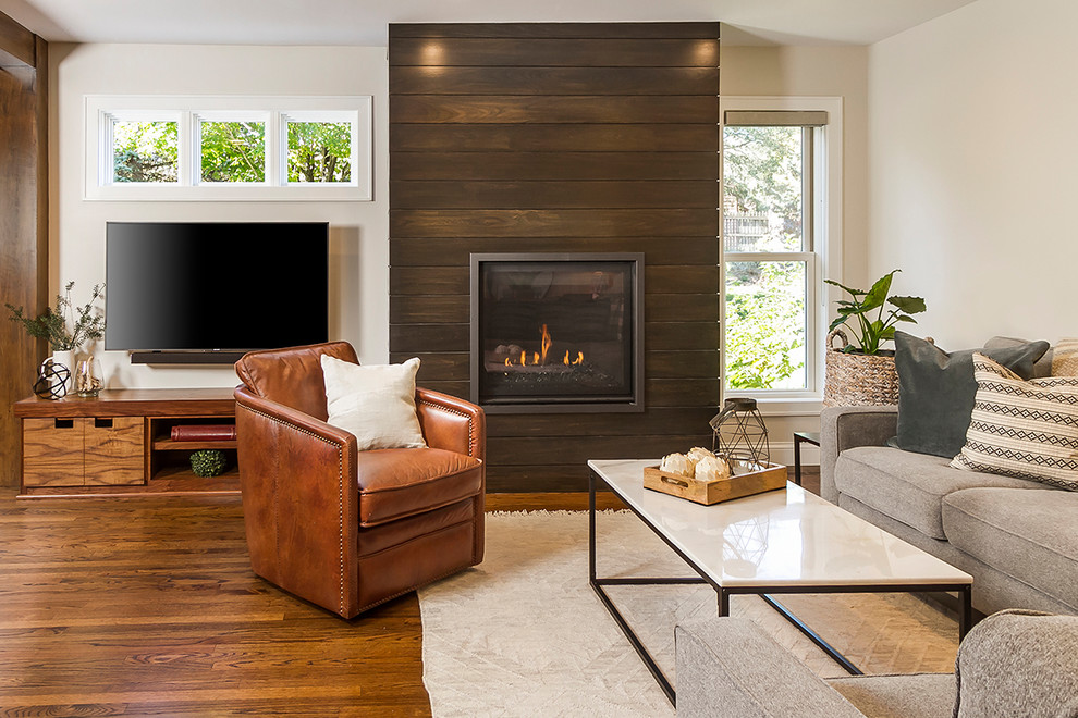 This is an example of a mid-sized transitional family room in Minneapolis with white walls, medium hardwood floors, a wood fireplace surround and a wall-mounted tv.
