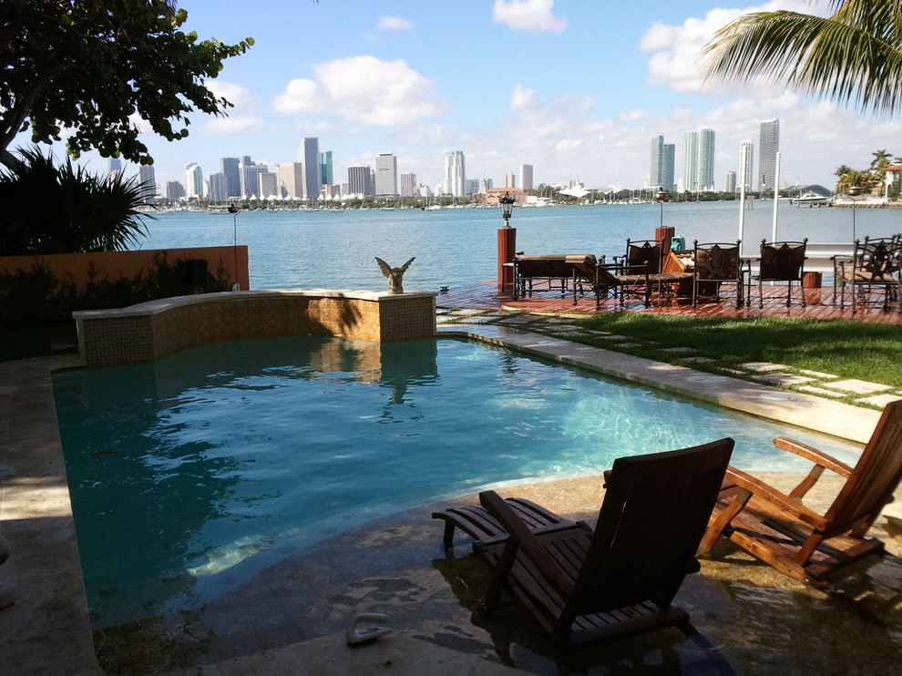 Photo of a small contemporary backyard custom-shaped natural pool in Miami with a water feature and natural stone pavers.