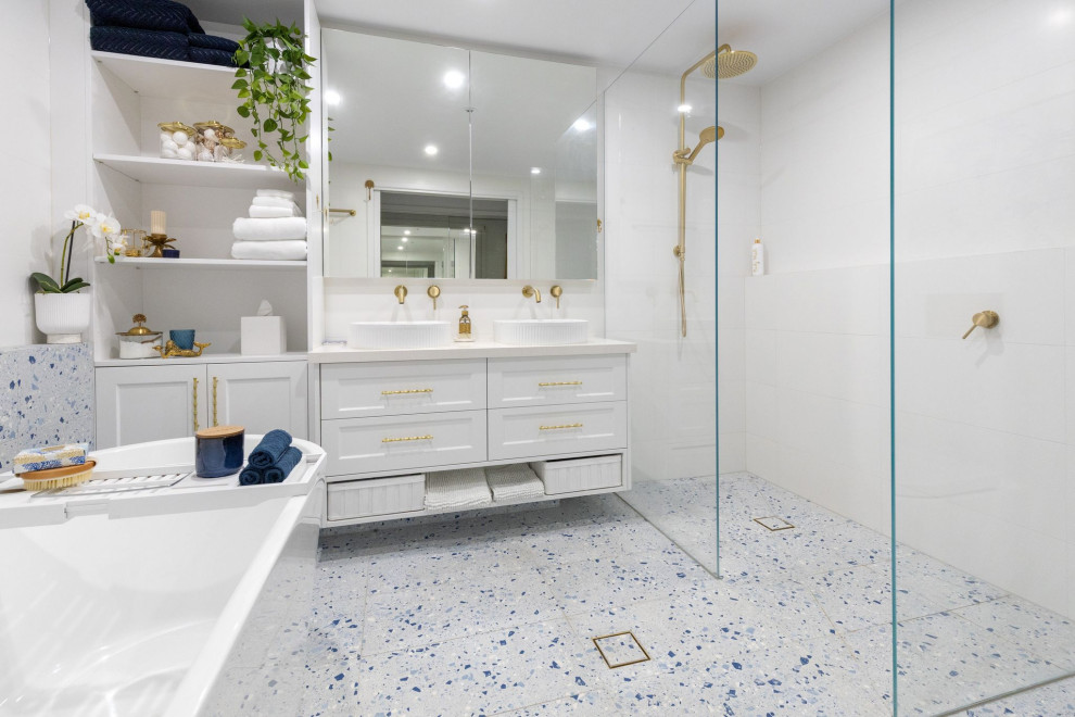 Пример оригинального дизайна: большая главная ванная комната в стиле модернизм с фасадами с филенкой типа жалюзи, белыми фасадами, отдельно стоящей ванной, открытым душем, инсталляцией, белой плиткой, керамогранитной плиткой, белыми стенами, полом из керамогранита, настольной раковиной, столешницей из искусственного кварца, синим полом, открытым душем, белой столешницей, нишей, тумбой под две раковины и подвесной тумбой