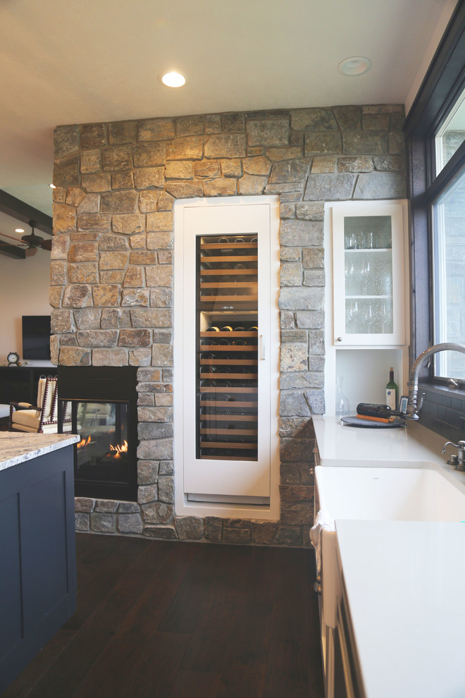 Example of a mid-sized transitional l-shaped dark wood floor eat-in kitchen design with a farmhouse sink, recessed-panel cabinets, white cabinets, granite countertops, black backsplash, porcelain backsplash, stainless steel appliances and an island