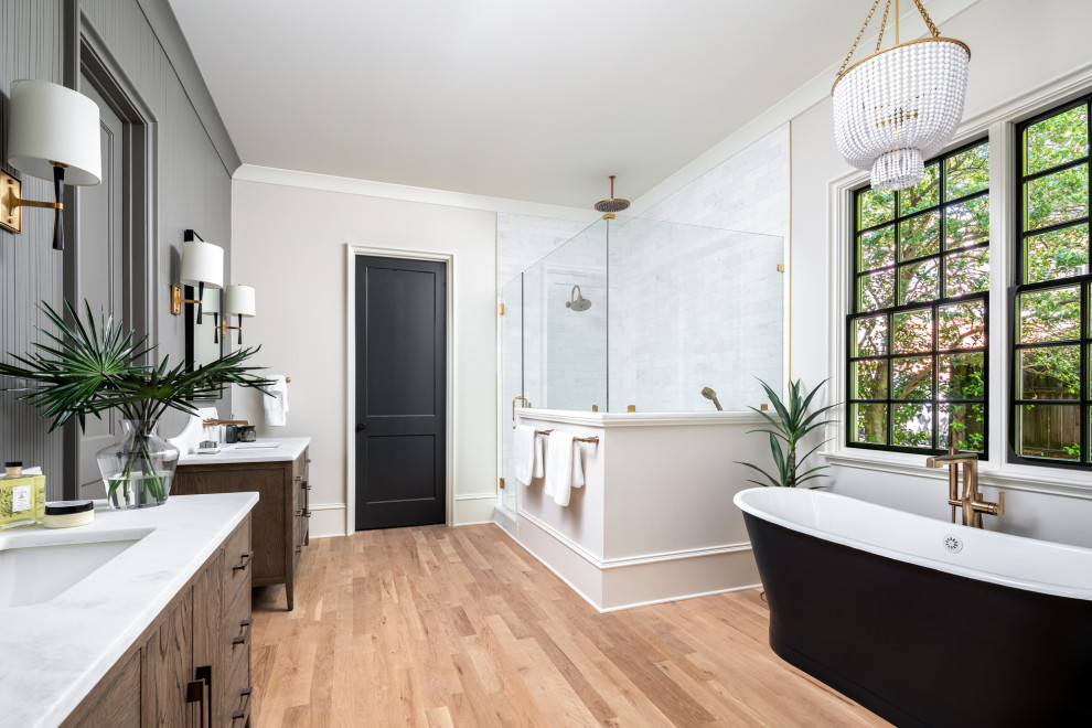На фото: большая главная ванная комната в стиле неоклассика (современная классика) с коричневыми фасадами, отдельно стоящей ванной, угловым душем, белой плиткой, белыми стенами, паркетным полом среднего тона, тумбой под две раковины и напольной тумбой
