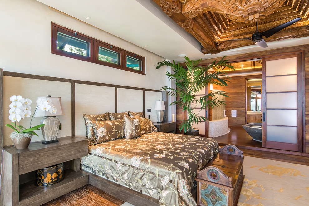 This is an example of a tropical master bedroom in Hawaii with white walls, medium hardwood floors and no fireplace.