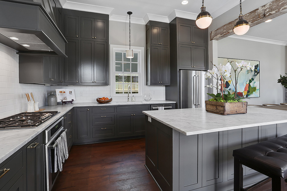 This is an example of a large traditional l-shaped open plan kitchen in New Orleans with a drop-in sink, recessed-panel cabinets, grey cabinets, granite benchtops, white splashback, ceramic splashback, stainless steel appliances, medium hardwood floors and with island.
