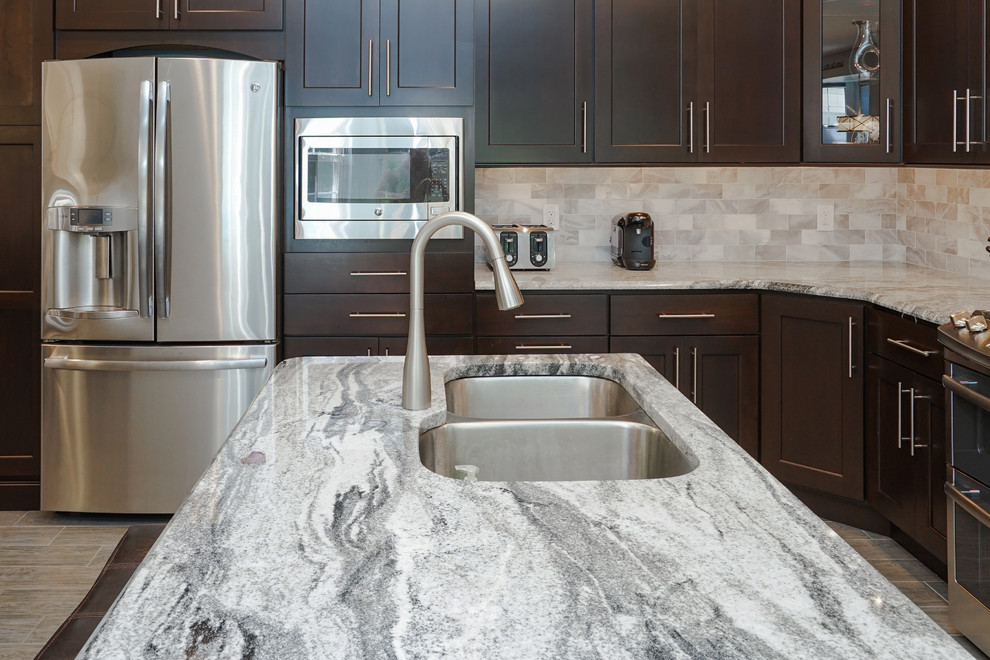 Inspiration for a large transitional l-shaped eat-in kitchen in Philadelphia with a double-bowl sink, granite benchtops, grey splashback, stone tile splashback, stainless steel appliances, with island, shaker cabinets, dark wood cabinets, vinyl floors and brown floor.