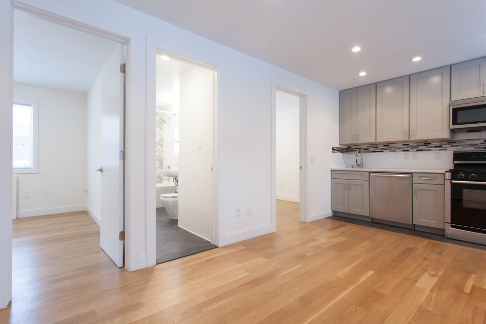 Photo of a large contemporary eat-in kitchen in New York with a drop-in sink, ceramic splashback, stainless steel appliances, light hardwood floors, no island and brown floor.