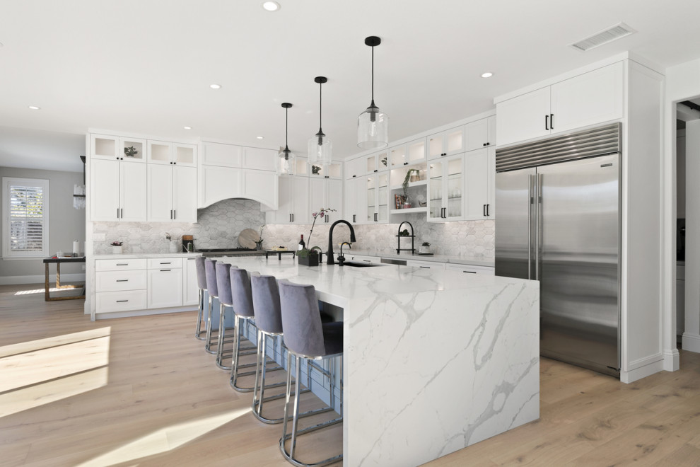 Inspiration for a large coastal l-shaped open plan kitchen in San Diego with a submerged sink, shaker cabinets, white cabinets, engineered stone countertops, grey splashback, marble splashback, light hardwood flooring, an island, beige floors and white worktops.