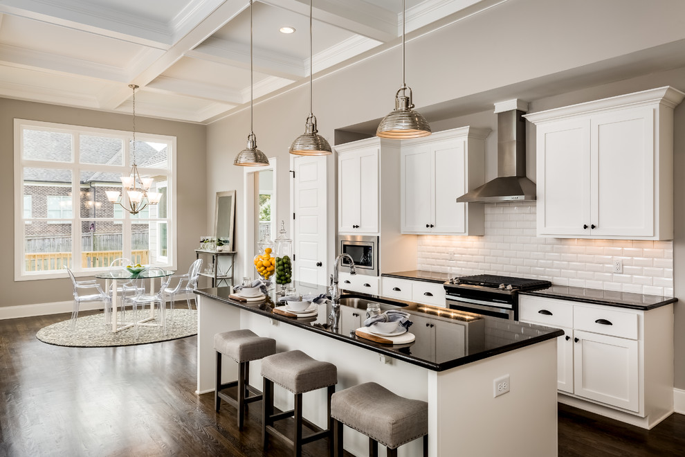 Photo of a mid-sized contemporary l-shaped open plan kitchen in Nashville with a farmhouse sink, shaker cabinets, granite benchtops, white splashback, subway tile splashback, stainless steel appliances, dark hardwood floors, with island, brown floor and black benchtop.