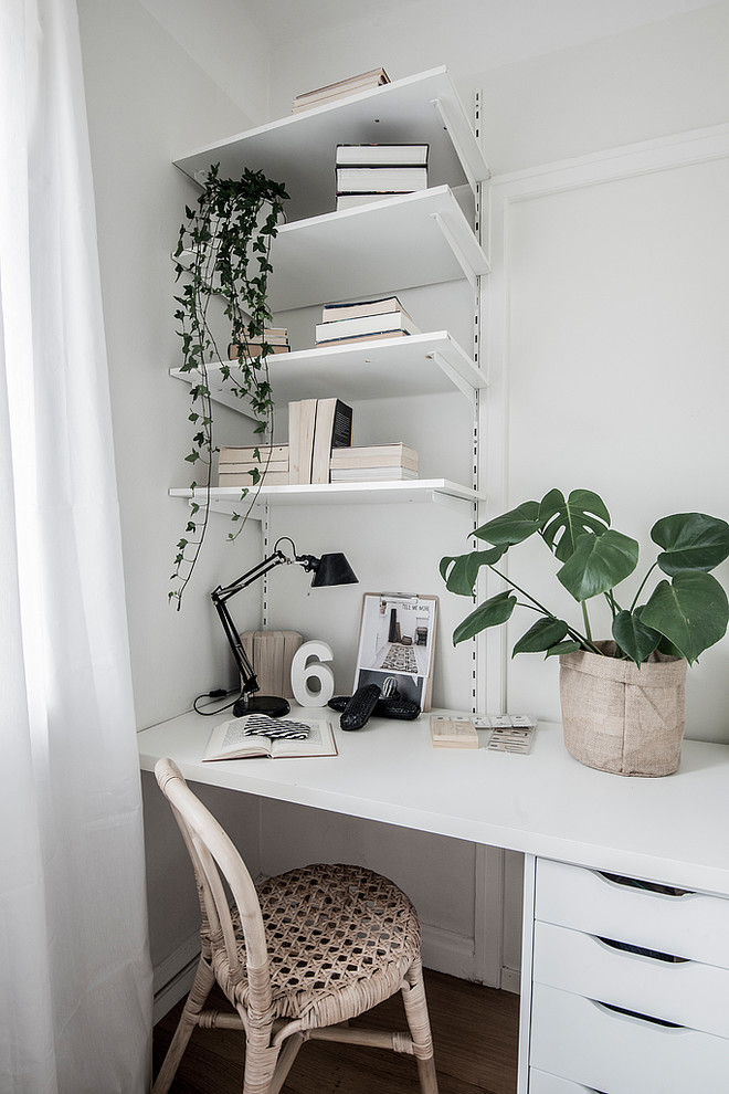 Photo of a scandinavian home office in Stockholm with white walls, dark hardwood floors, a built-in desk and brown floor.