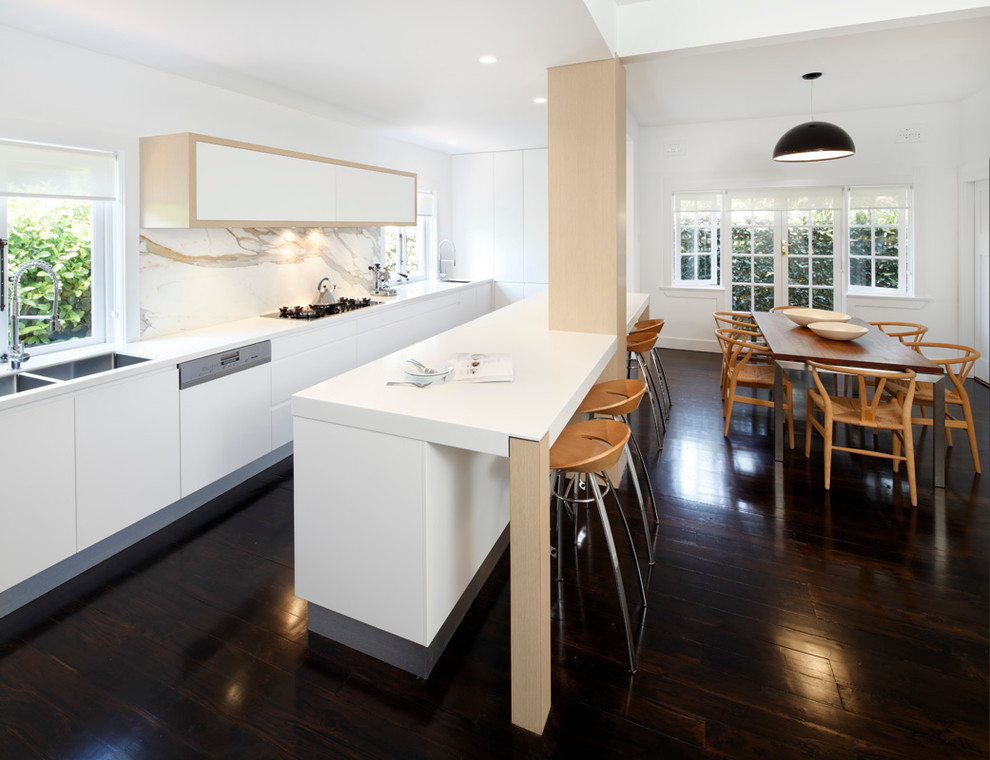 Design ideas for a modern single-wall eat-in kitchen in Sydney with a drop-in sink, flat-panel cabinets, white cabinets, solid surface benchtops, stone slab splashback, stainless steel appliances and white splashback.