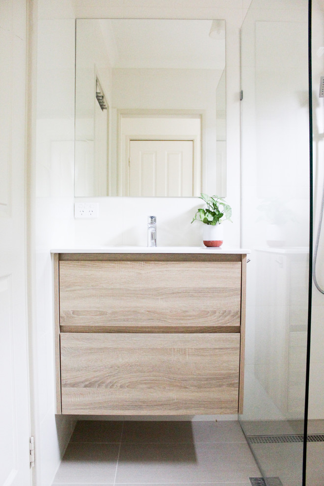 Inspiration for a small 3/4 bathroom in Perth with flat-panel cabinets, light wood cabinets, an open shower, a one-piece toilet, beige tile, ceramic tile, beige walls, porcelain floors, an integrated sink, solid surface benchtops, beige floor and white benchtops.