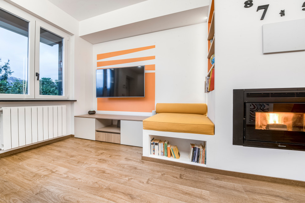 На фото: открытая гостиная комната среднего размера в современном стиле с с книжными шкафами и полками, оранжевыми стенами, светлым паркетным полом, стандартным камином, фасадом камина из штукатурки, телевизором на стене и коричневым полом
