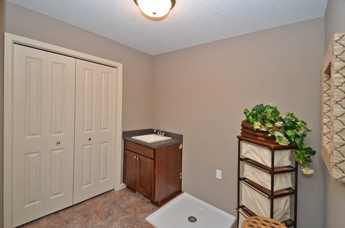 Mid-sized transitional linoleum floor dedicated laundry room photo in Minneapolis with a drop-in sink, shaker cabinets, medium tone wood cabinets, laminate countertops and beige walls