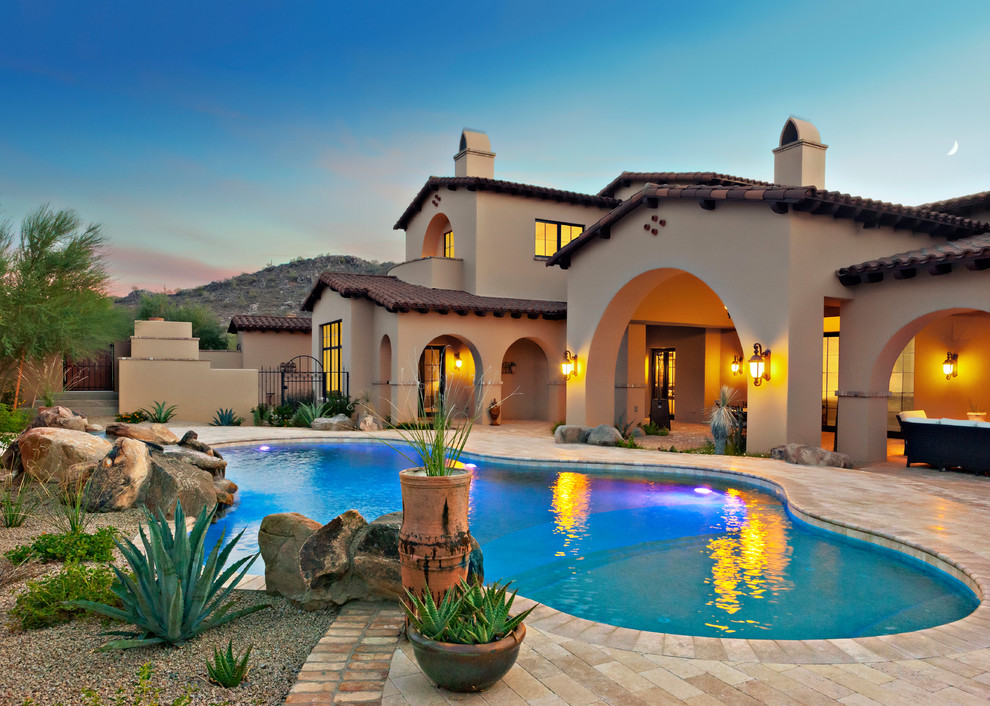 Large mediterranean backyard custom-shaped pool in Phoenix with brick pavers.