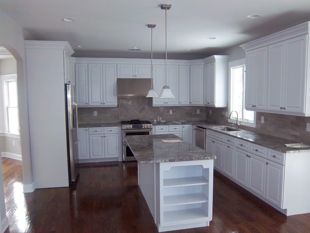 Large transitional u-shaped dark wood floor and brown floor kitchen photo with an undermount sink, raised-panel cabinets, white cabinets, granite countertops, gray backsplash, porcelain backsplash, stainless steel appliances, an island and gray countertops
