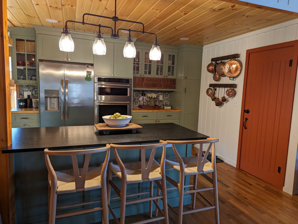 Eat-in kitchen - mid-sized rustic l-shaped medium tone wood floor, brown floor and wood ceiling eat-in kitchen idea with a farmhouse sink, shaker cabinets, green cabinets, granite countertops, multicolored backsplash, ceramic backsplash, stainless steel appliances and black countertops