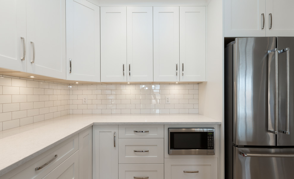 Open concept kitchen - mid-sized transitional l-shaped light wood floor open concept kitchen idea with an undermount sink, shaker cabinets, white cabinets, quartz countertops, white backsplash, subway tile backsplash, stainless steel appliances, an island and white countertops