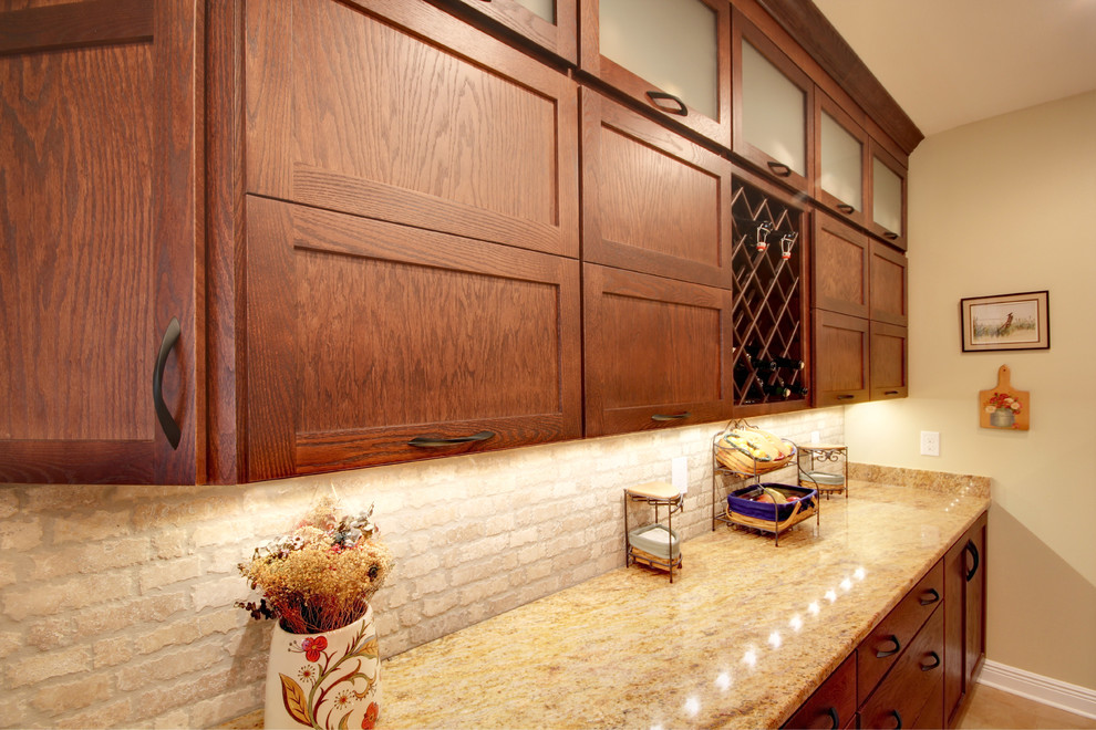 Example of a transitional eat-in kitchen design in Miami with an undermount sink, shaker cabinets, brown cabinets, granite countertops, beige backsplash, stone tile backsplash and stainless steel appliances