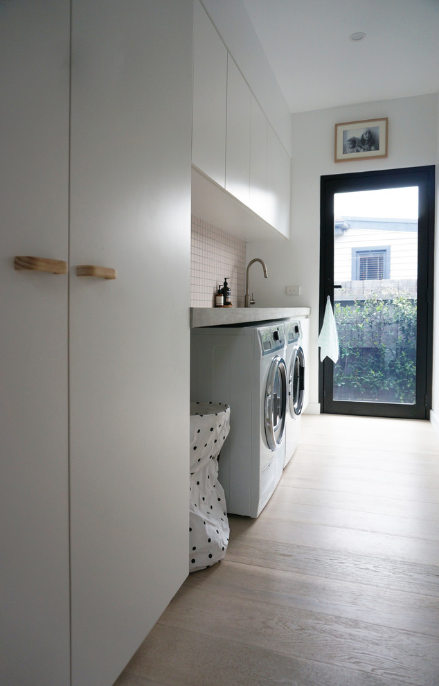Design ideas for a small contemporary single-wall dedicated laundry room in Melbourne with an undermount sink, concrete benchtops, a side-by-side washer and dryer, flat-panel cabinets, white cabinets, light hardwood floors and white walls.