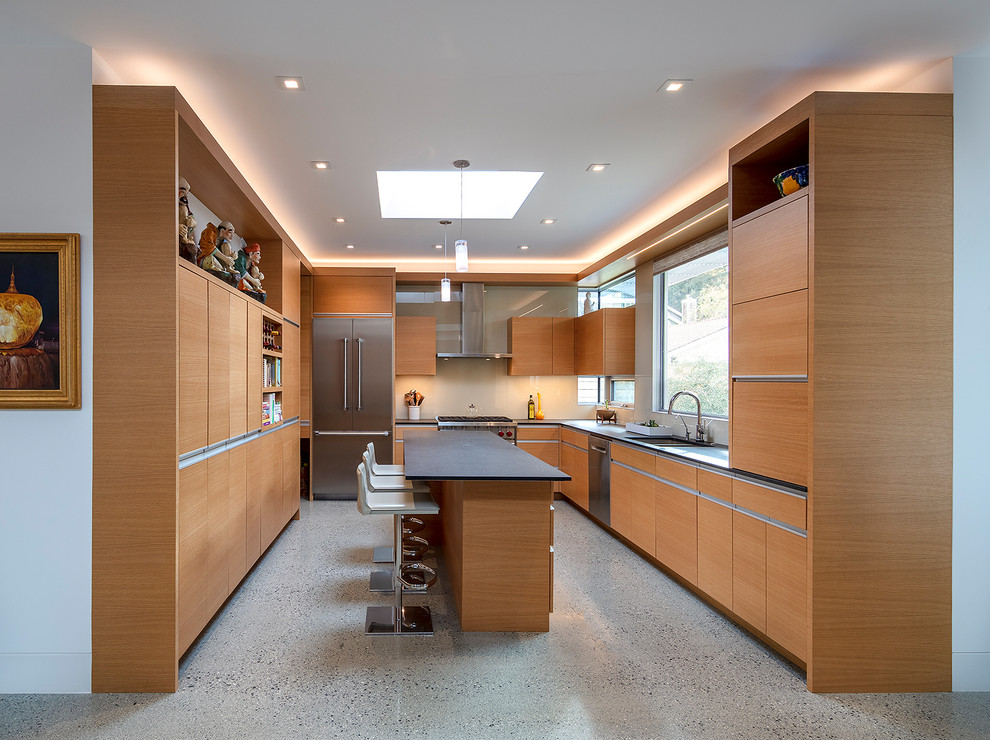 Design ideas for a midcentury u-shaped kitchen in San Francisco with a double-bowl sink, flat-panel cabinets, light wood cabinets, white splashback, stainless steel appliances, with island, grey floor and black benchtop.
