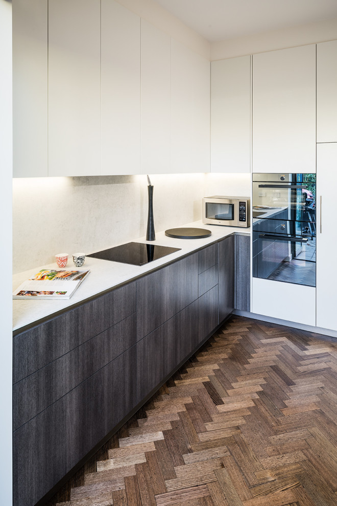 Small contemporary l-shaped eat-in kitchen in Melbourne with a drop-in sink, flat-panel cabinets, dark wood cabinets, white splashback, stone slab splashback, panelled appliances, medium hardwood floors, with island, brown floor and white benchtop.