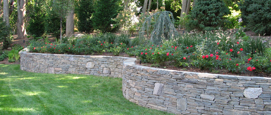 STACKED STONE WALL WITH LARGER PIECES OF ROUND AND IRREGULAR STONE ADDED TO BREAK UP COMPOSTION.  We planted knock out roses and a blue atlas weeping spruce as a focal point. Peter Atkins and Associat