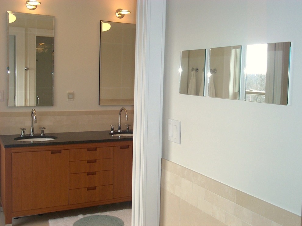This is an example of a large contemporary master bathroom in New York with flat-panel cabinets, medium wood cabinets, a one-piece toilet, beige tile, stone tile, beige walls, limestone floors, an undermount sink, granite benchtops, a drop-in tub, black benchtops, a double vanity and a freestanding vanity.
