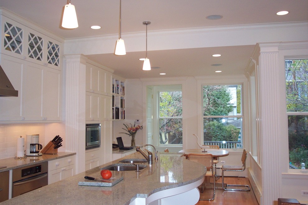Inspiration for a mid-sized transitional l-shaped medium tone wood floor and brown floor eat-in kitchen remodel in Chicago with an undermount sink, recessed-panel cabinets, white cabinets, white backsplash, subway tile backsplash, stainless steel appliances, an island and granite countertops