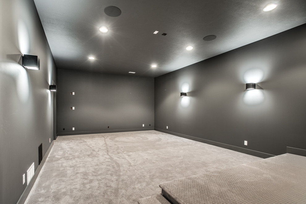 This is an example of a large country enclosed home theatre in Omaha with carpet, a projector screen, grey walls and beige floor.