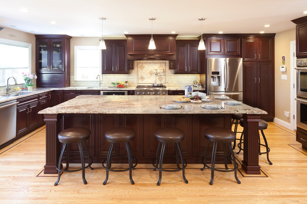 Photo of a large traditional l-shaped kitchen in San Francisco with raised-panel cabinets, dark wood cabinets, beige splashback, stainless steel appliances, an undermount sink, granite benchtops, medium hardwood floors, with island and travertine splashback.