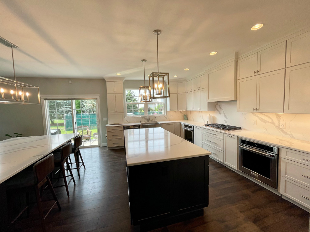 Example of a large transitional u-shaped medium tone wood floor and brown floor eat-in kitchen design in Chicago with a farmhouse sink, shaker cabinets, white cabinets, quartz countertops, white backsplash, quartz backsplash, stainless steel appliances, two islands and white countertops
