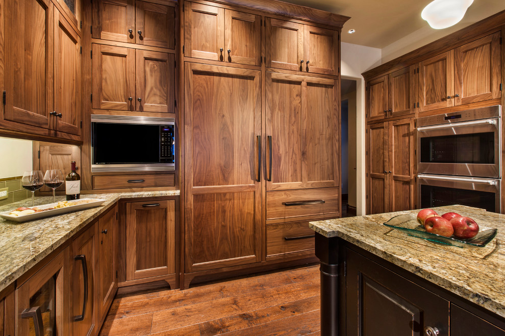 This is an example of an expansive traditional u-shaped eat-in kitchen in Denver with flat-panel cabinets, medium wood cabinets, with island, a single-bowl sink, granite benchtops, green splashback, glass tile splashback, panelled appliances and medium hardwood floors.