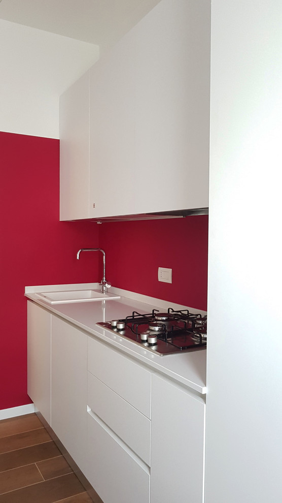 Design ideas for a mid-sized contemporary galley separate kitchen in Milan with a single-bowl sink, flat-panel cabinets, white cabinets, red splashback, porcelain floors, no island, brown floor, white benchtop, quartzite benchtops and stainless steel appliances.