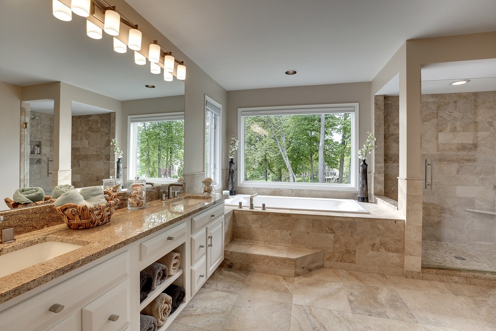 This is an example of a large traditional master bathroom in Minneapolis with an undermount sink, raised-panel cabinets, white cabinets, granite benchtops, a drop-in tub, a corner shower, a two-piece toilet, brown tile, stone tile and brown walls.